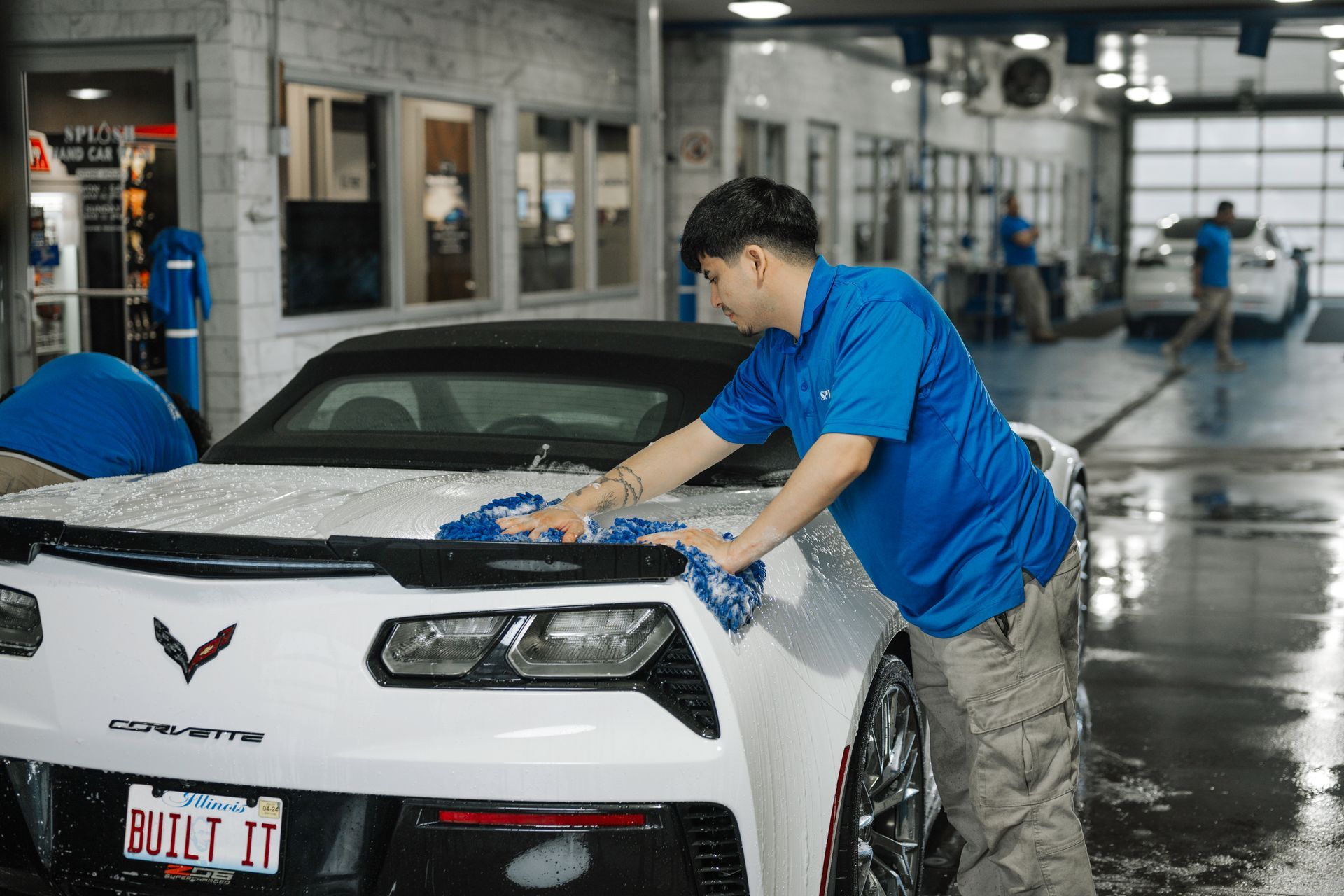 A man in a blue shirt is washing a white sports car.