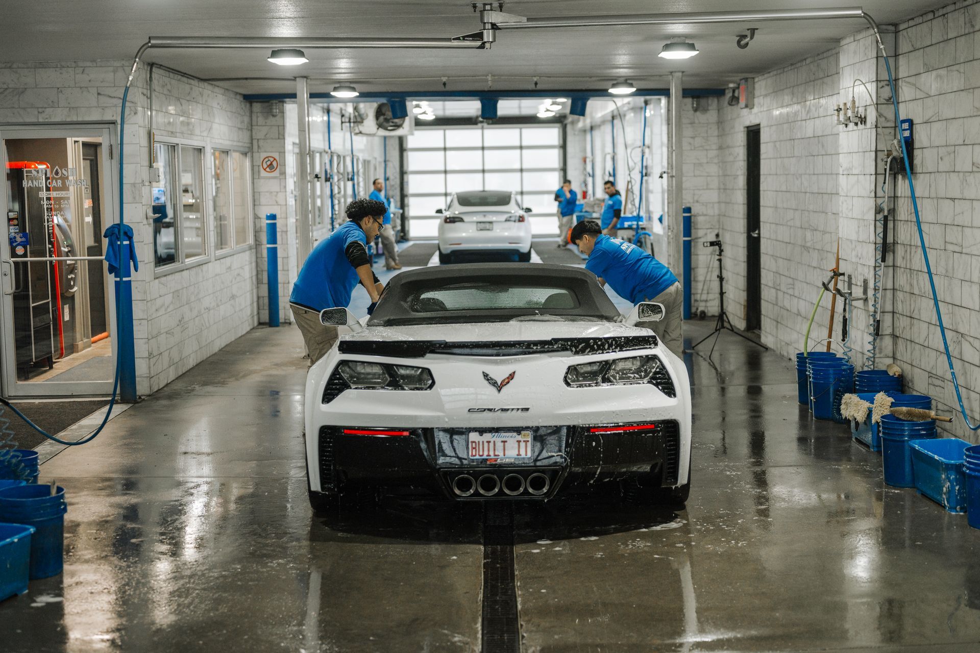 A white corvette is being washed in a car wash.