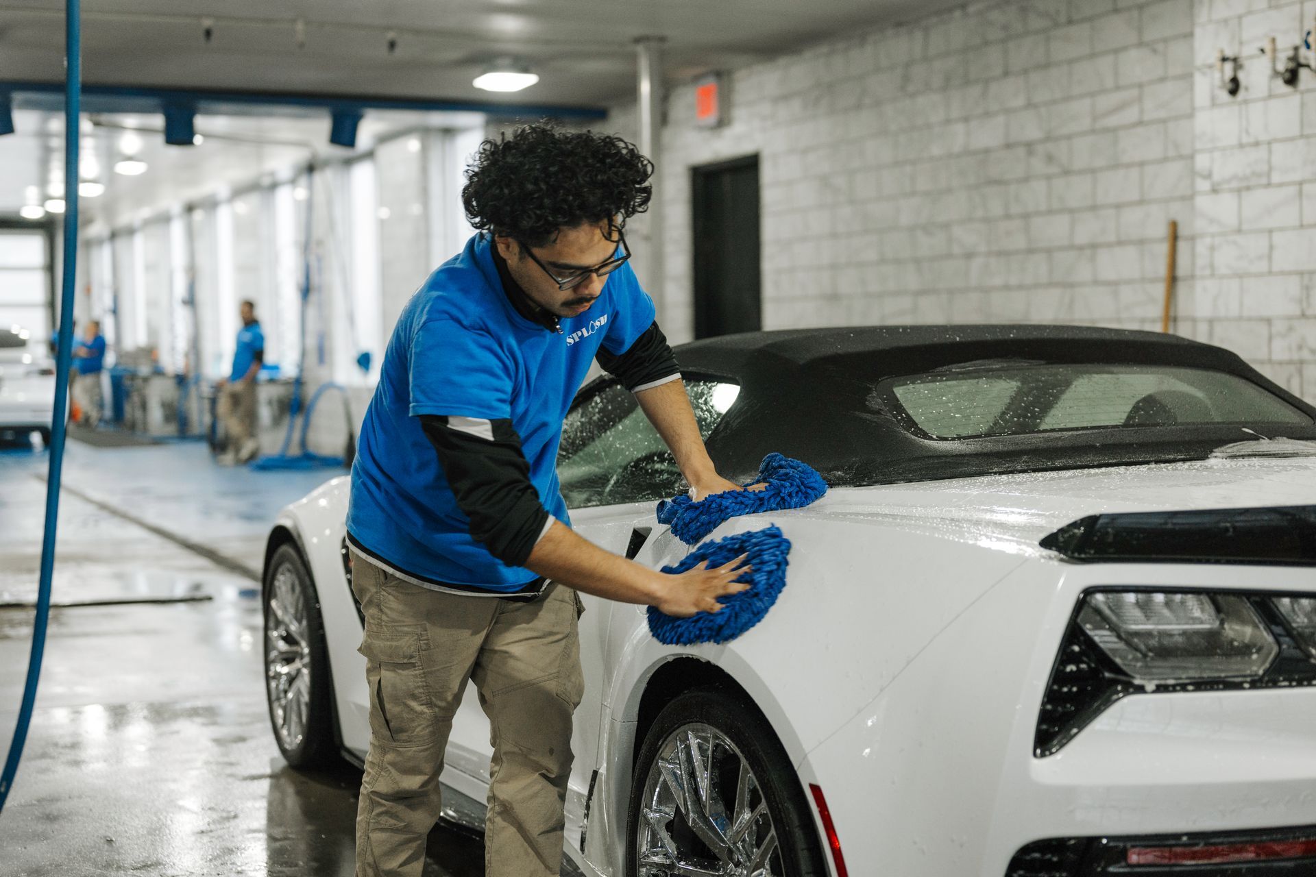 A man is cleaning a white sports car with a blue cloth.