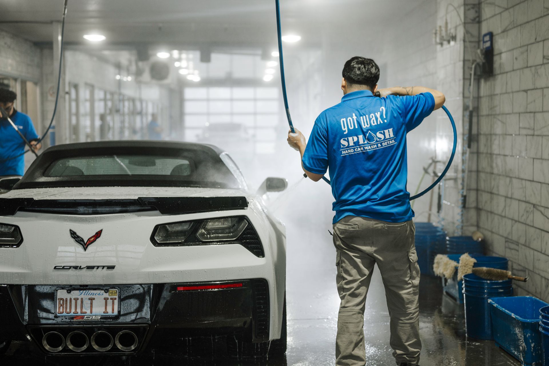 A man is washing a white corvette in a car wash.