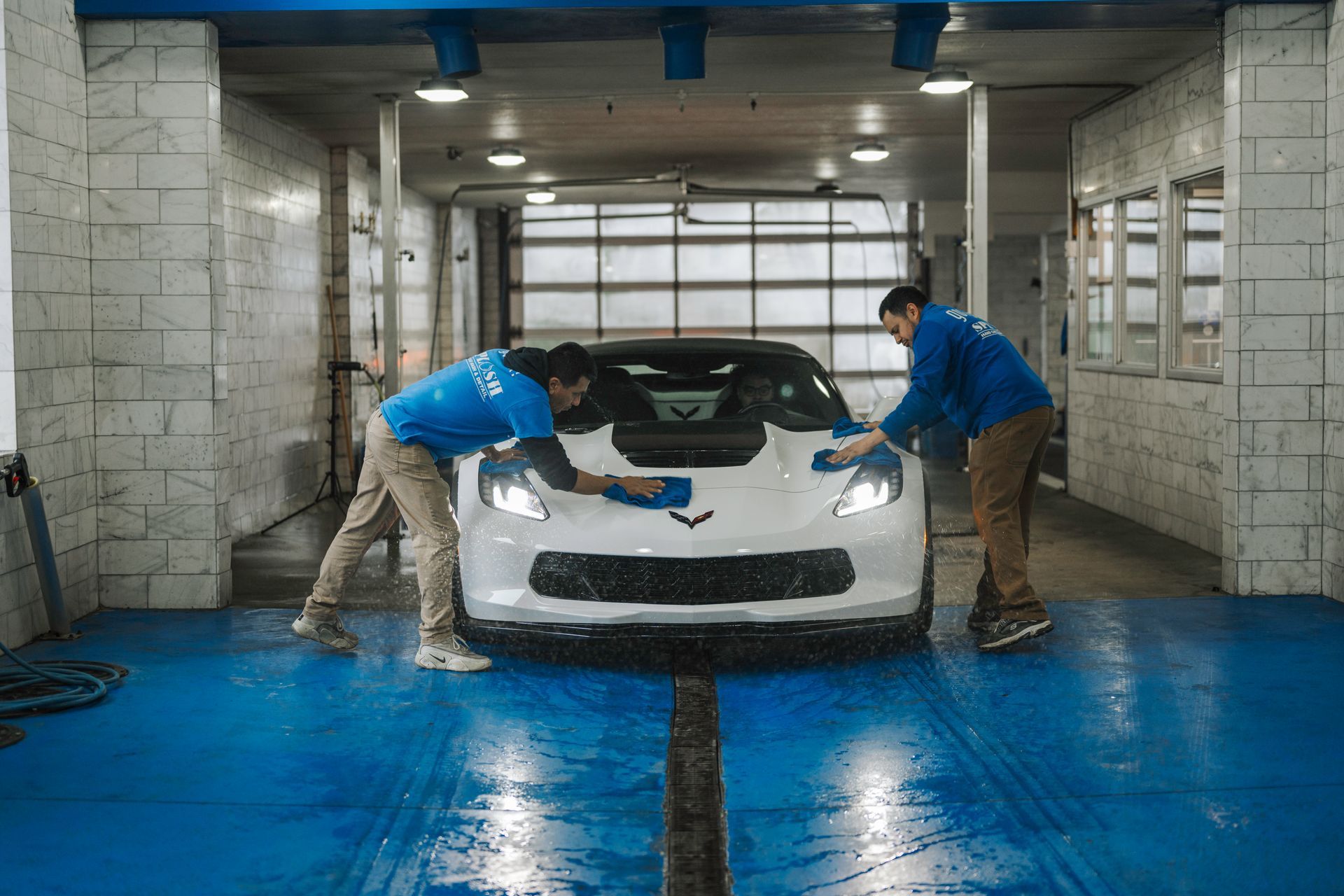 Two men are washing a white sports car in a car wash.