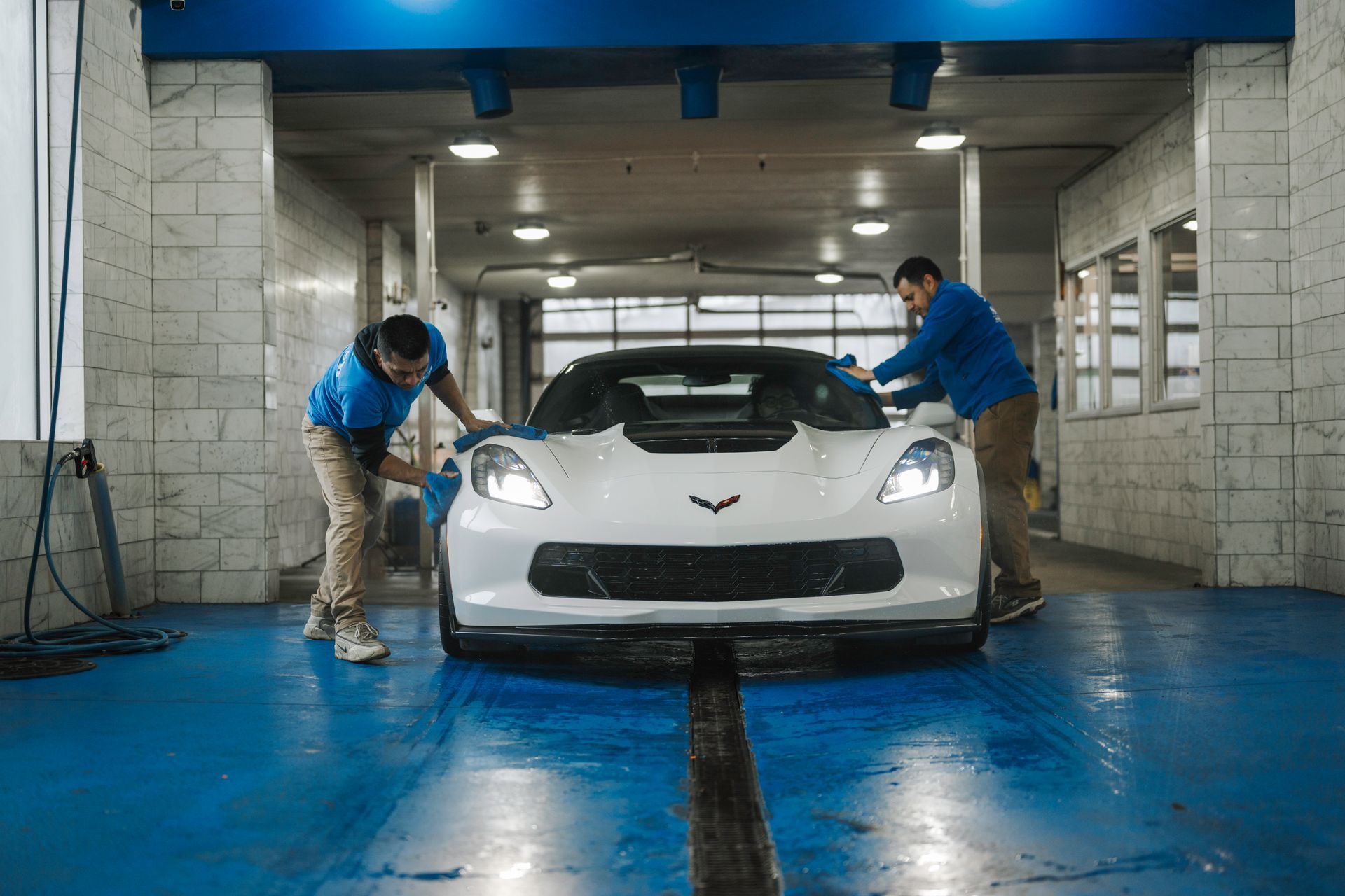 Two men are cleaning a white sports car in a car wash.