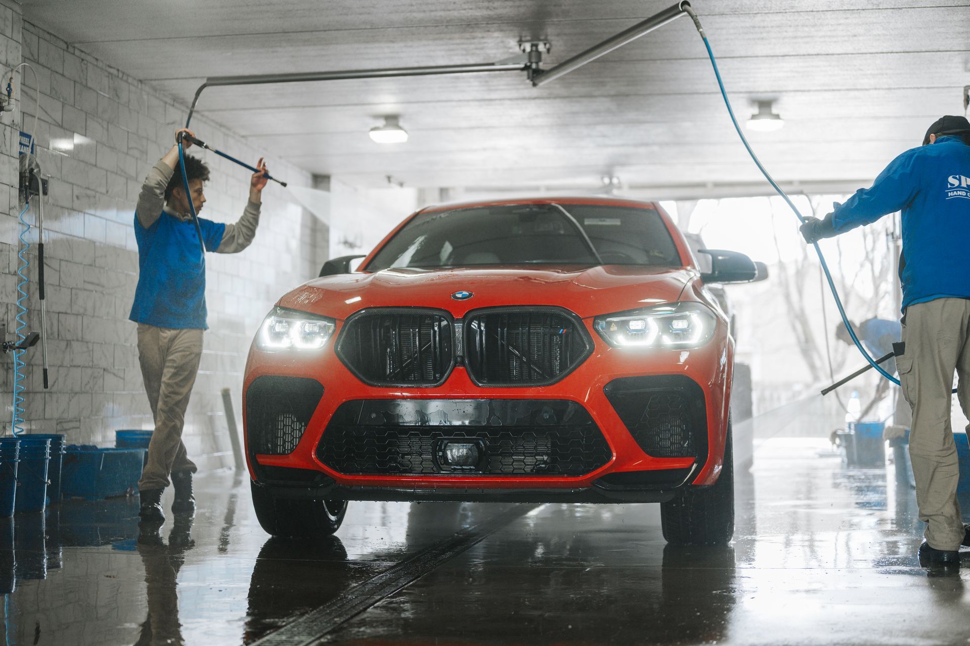A red bmw x6 m is being washed by two men in a car wash.
