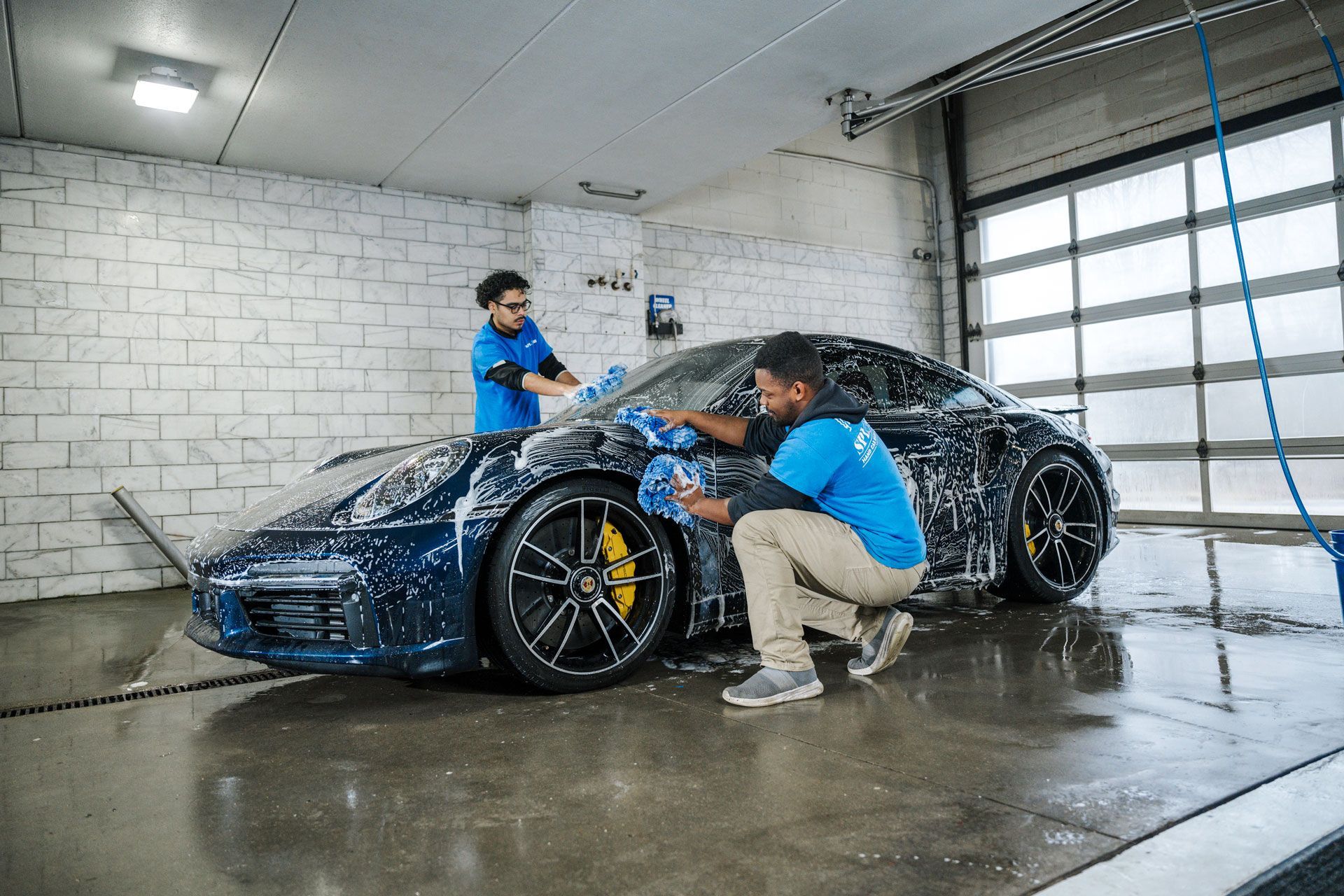 Two men are washing a sports car in a car wash.