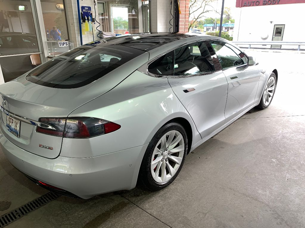 A silver tesla model s is parked in front of a car wash.