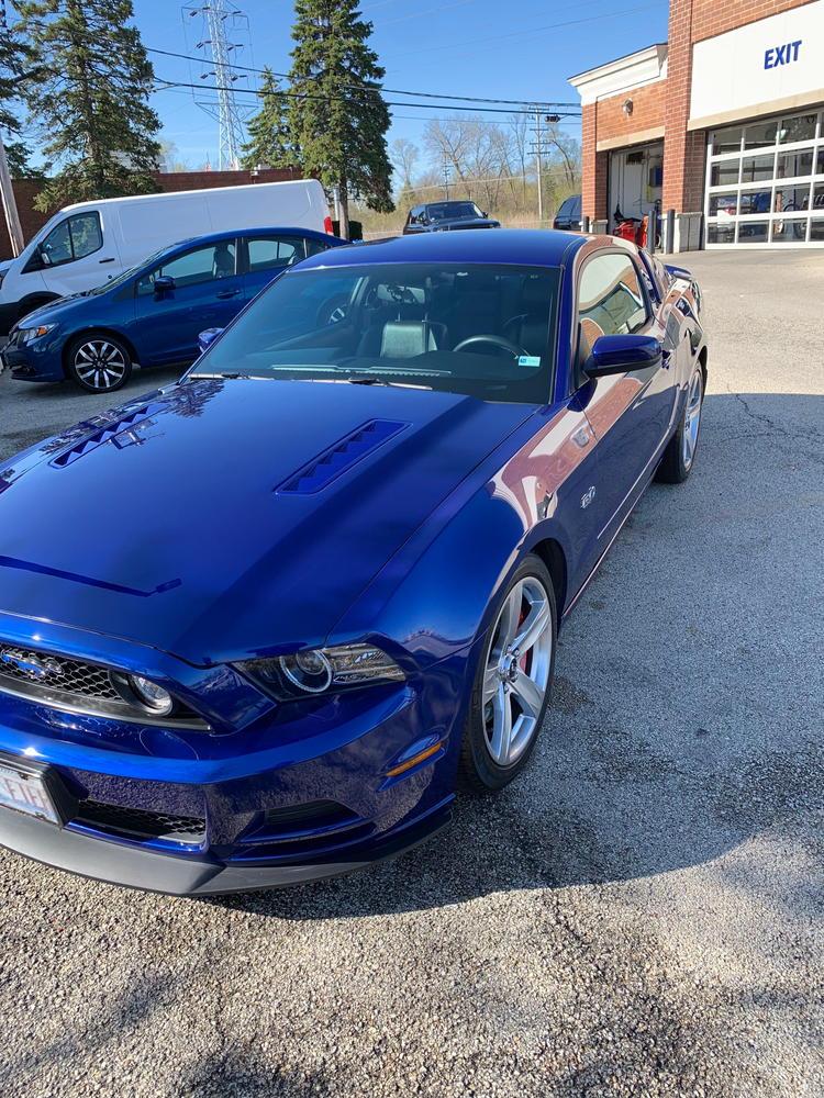 A blue mustang is parked in front of a garage.