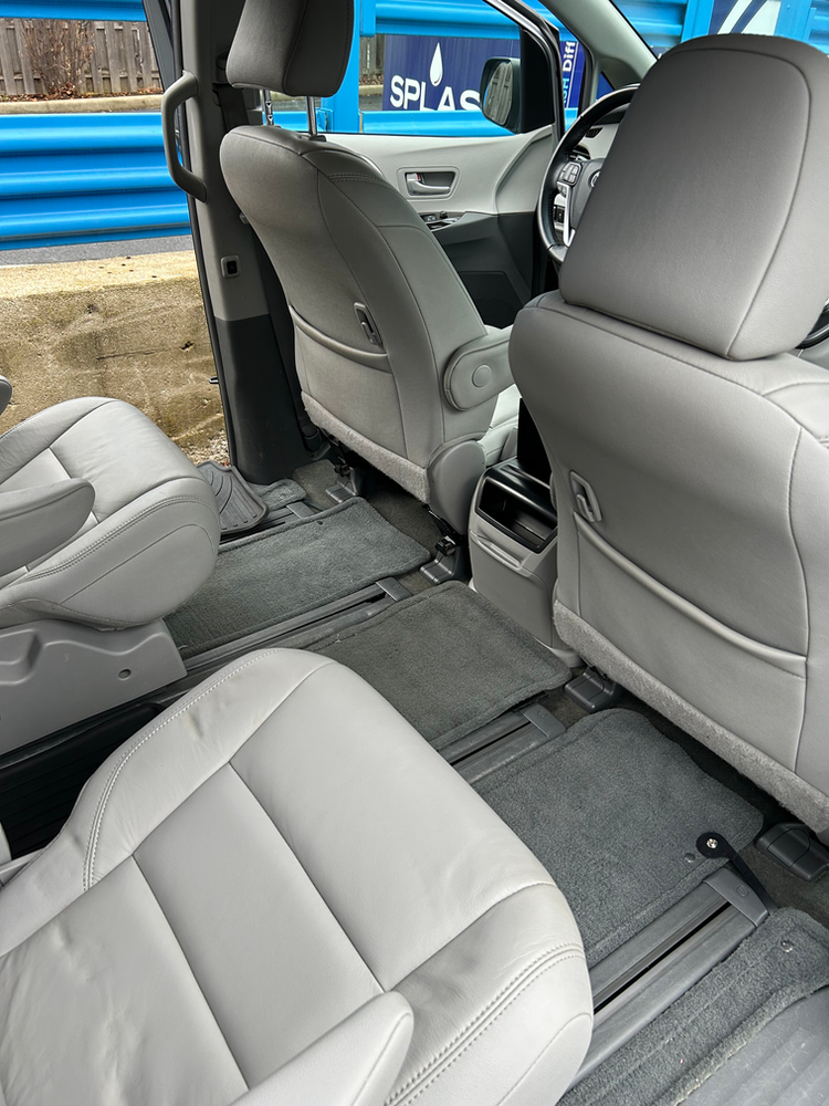 The interior of a minivan with white leather seats and a blue dumpster in the background.