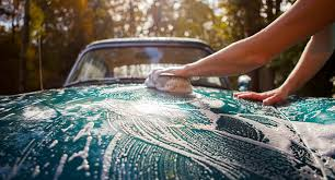 A woman is washing a blue car with a sponge.