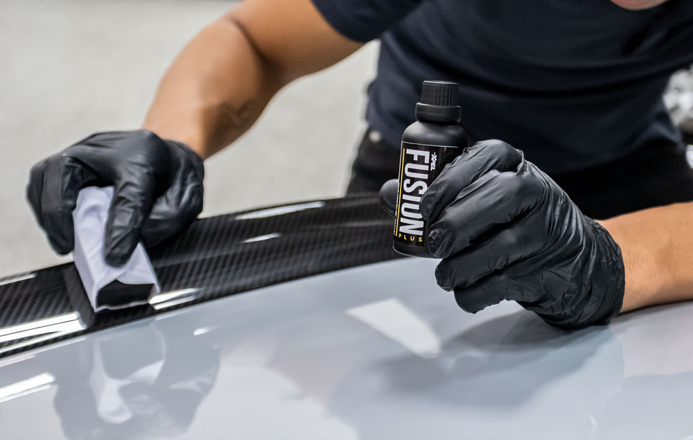 A man wearing black gloves is applying a coating to a car.