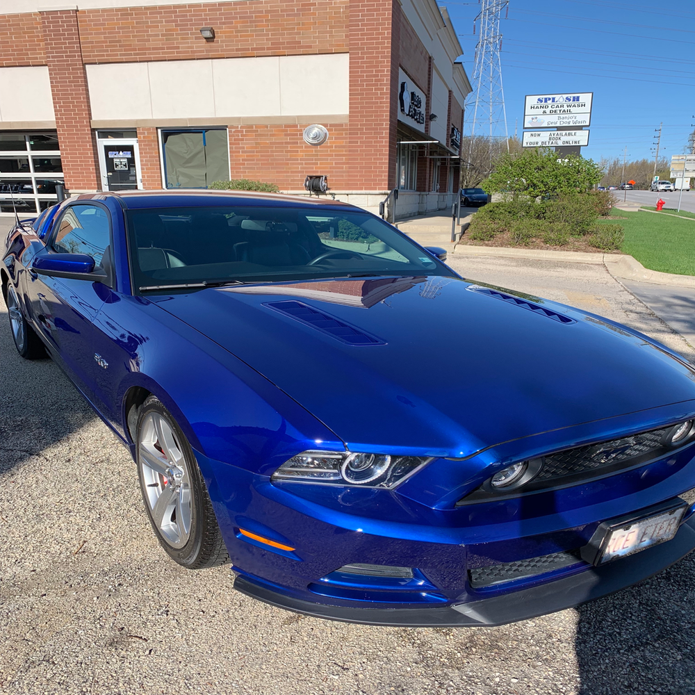 A blue mustang is parked in front of a brick building