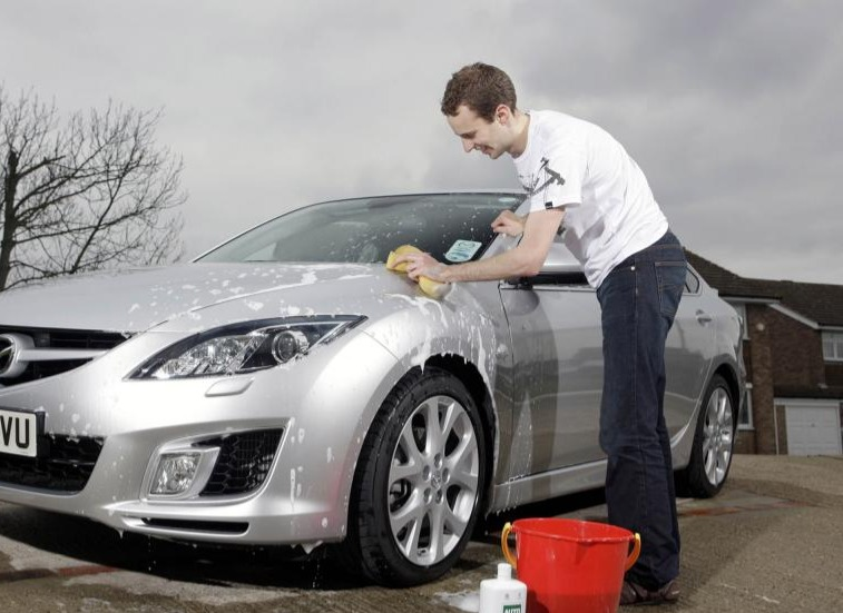 A man is washing a silver car with a yellow sponge