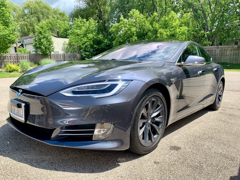 A tesla model s is parked in a driveway in front of a fence.