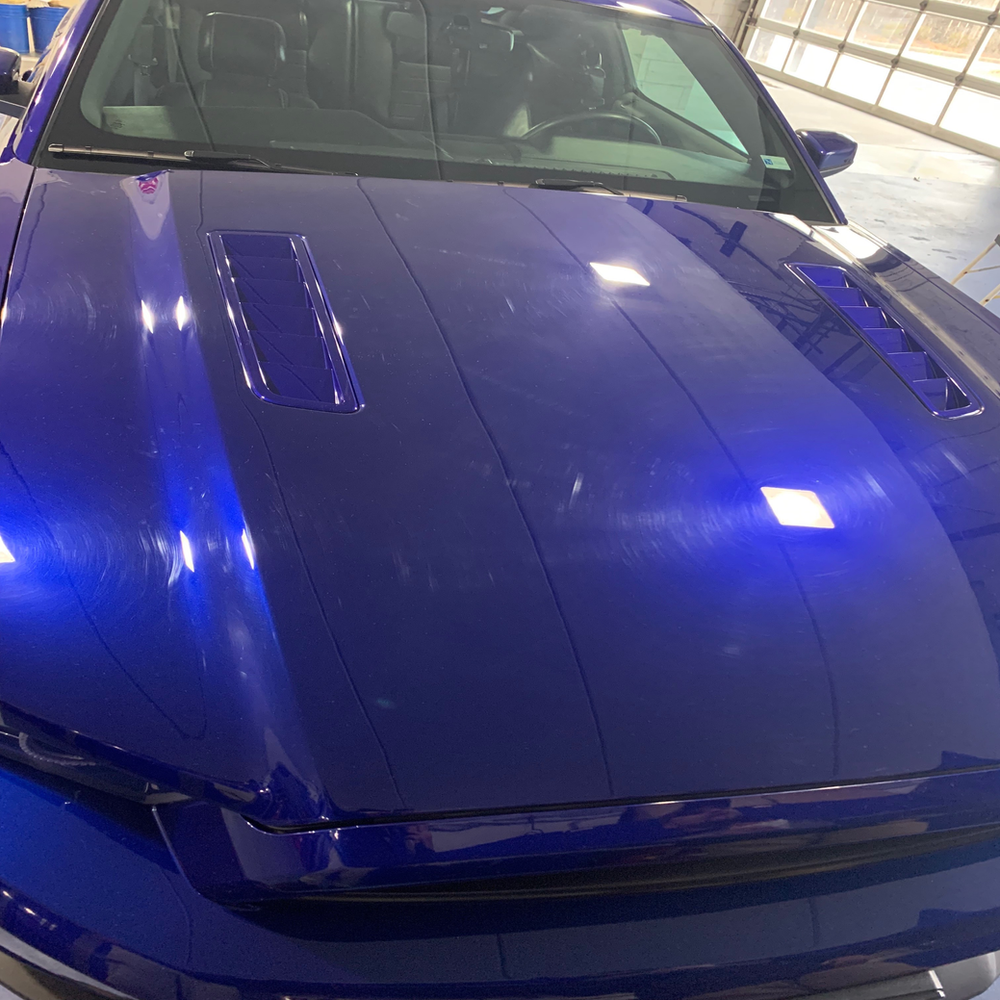 A blue car with the hood up is parked in a garage