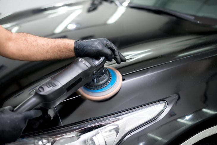 A man is polishing the hood of a car with a machine.