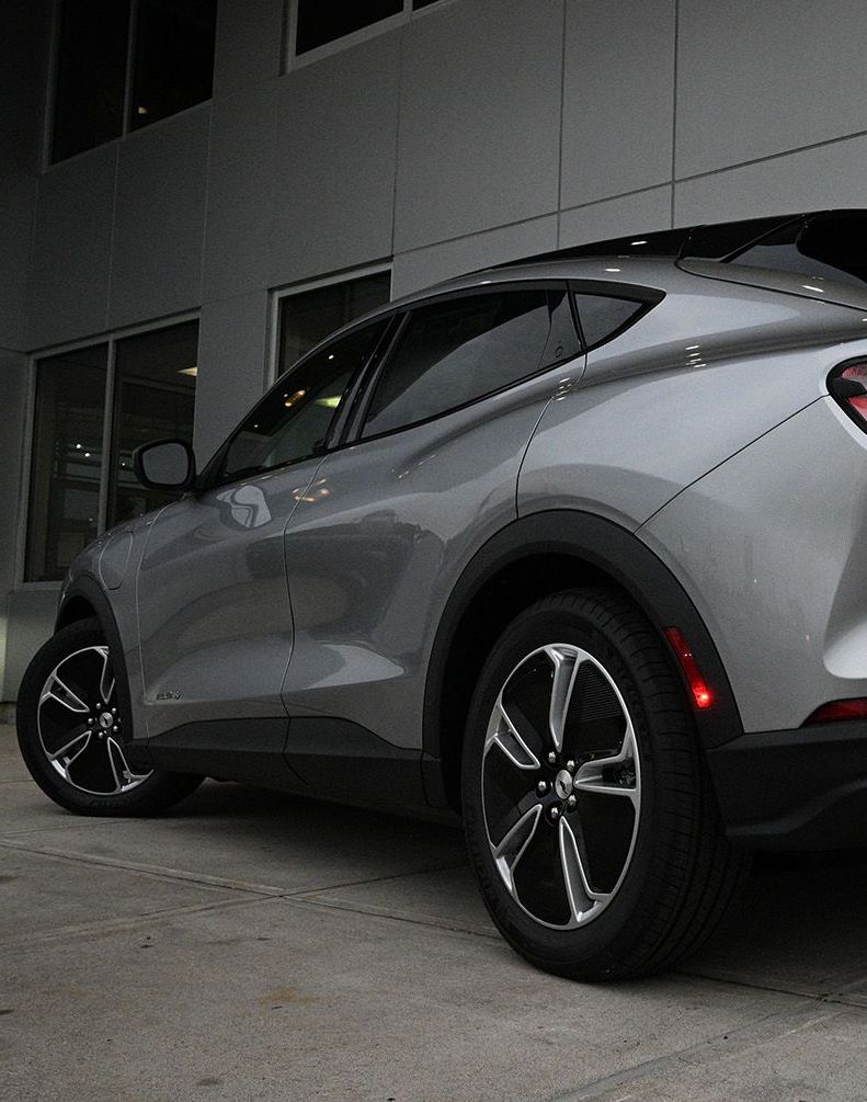 Silver Ford Mach-E parked in front of a building with black wheels and a red side marker.