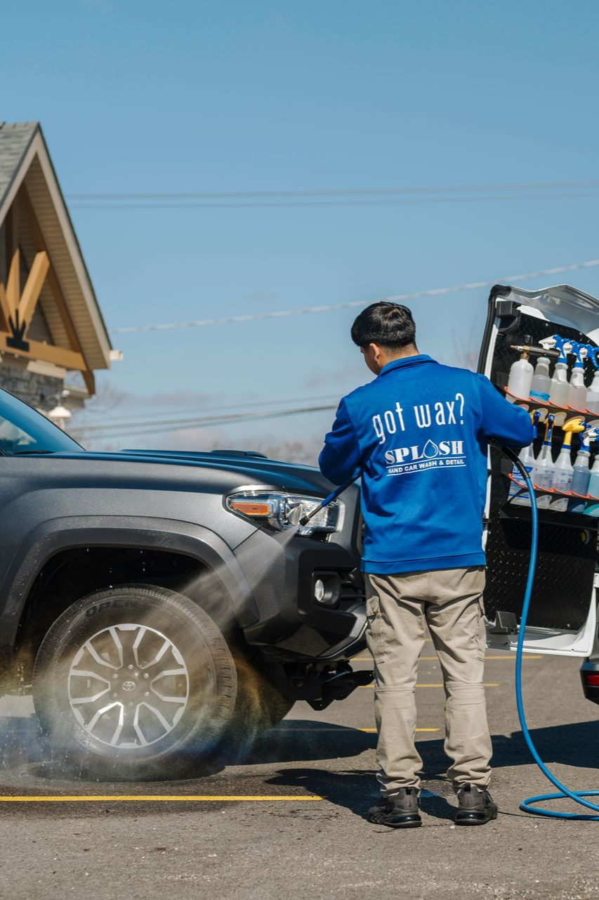 A man is washing a car next to a van.