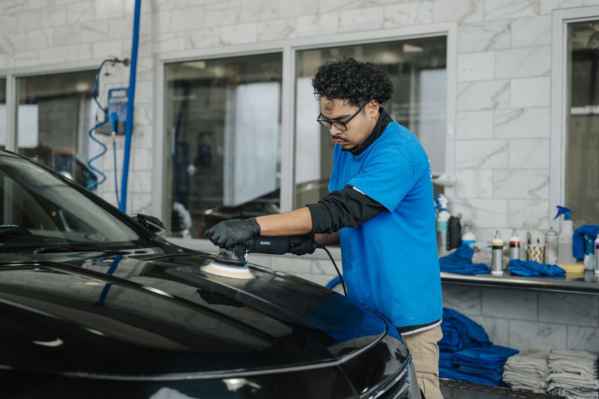 A man is polishing a black car in a car wash.