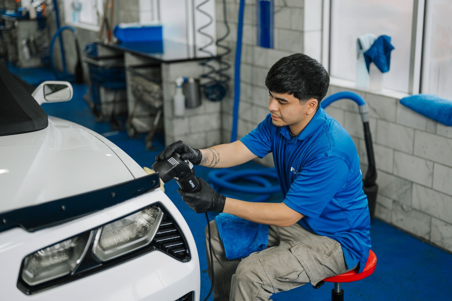 A man in a blue shirt is polishing a white car in a garage.