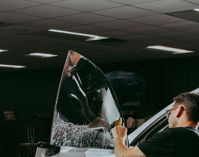 A man is applying tinted glass to a car window.