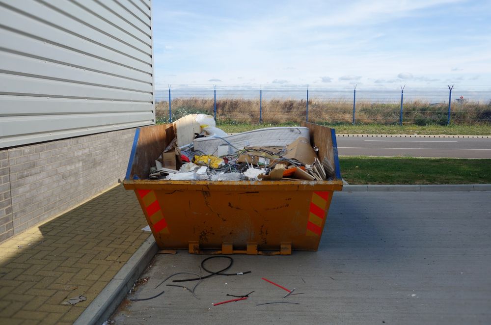 Large, Orange Dumpster Overflowing With Trash Next to a Building on a Sunny Day — Skip Bin Hire Sunshine Coast in Coolum, QLD