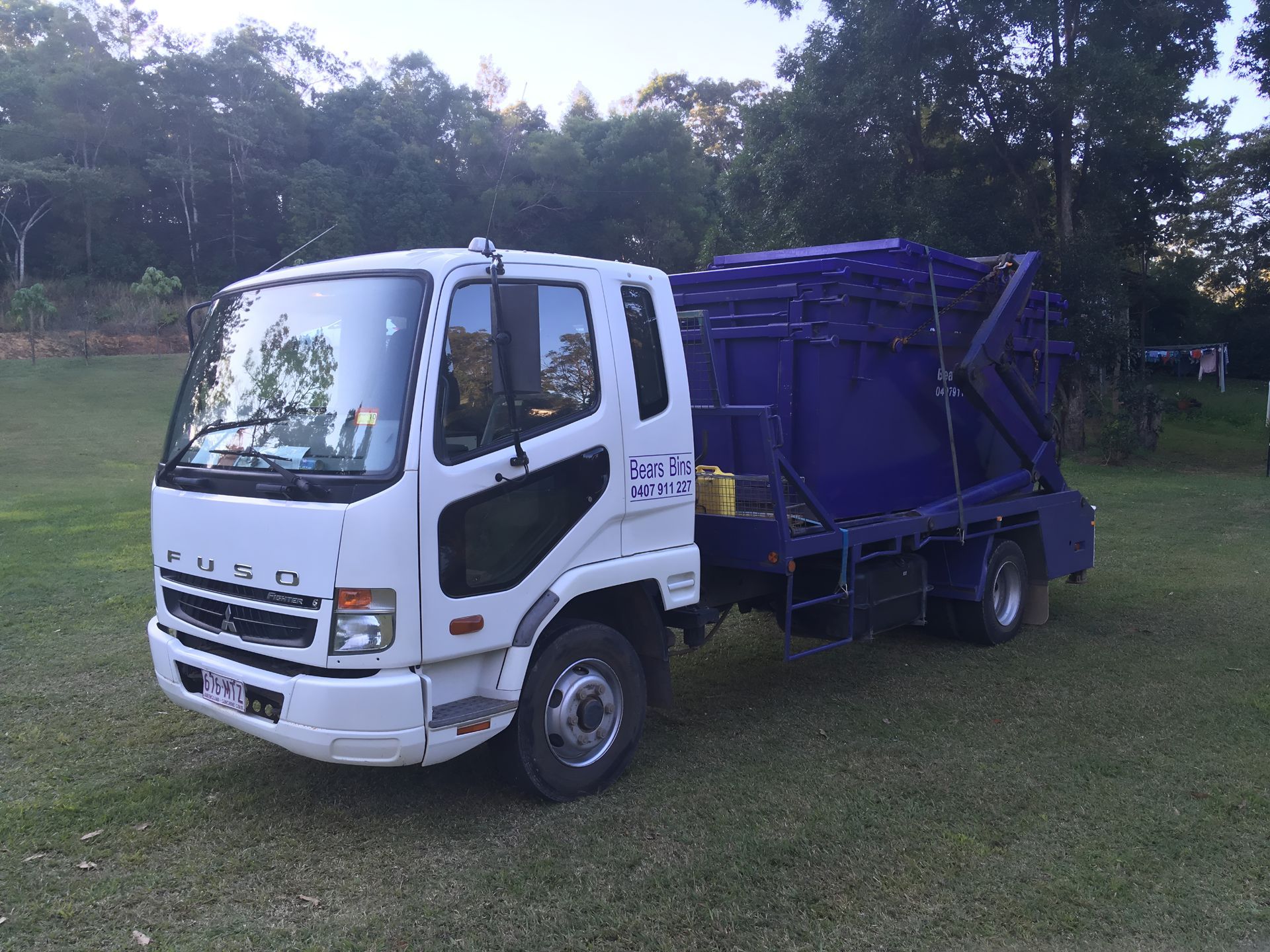 White Fuso Truck With a Blue Skip Bin on a Grassy Area, Trees in Background — Skip Bin Hire Sunshine Coast in Kin Kin, QLD
