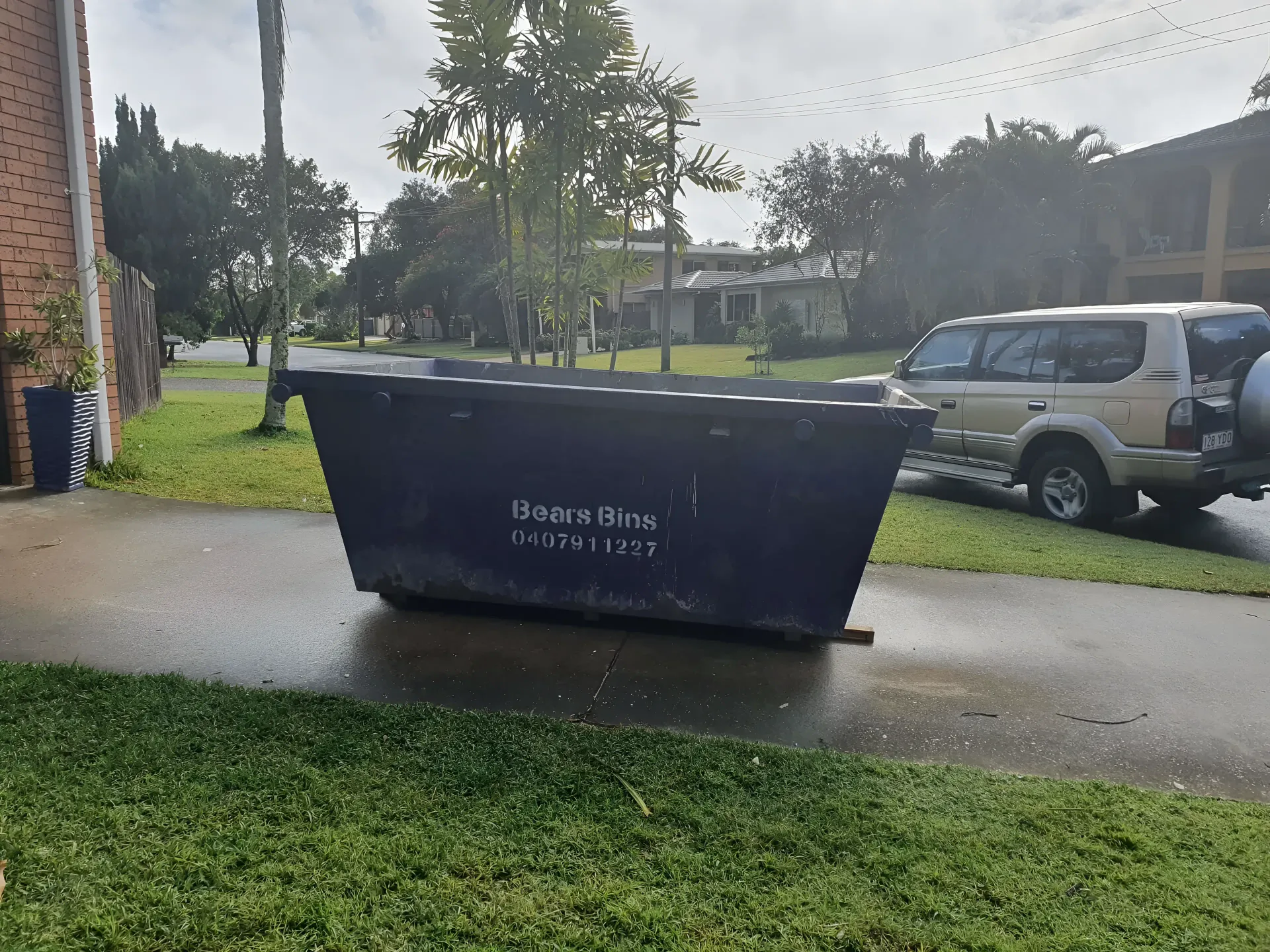 Large Black Dumpster on a Sidewalk Near a Street With a Parked Suv — Skip Bin Hire Sunshine Coast in Kin Kin, QLD