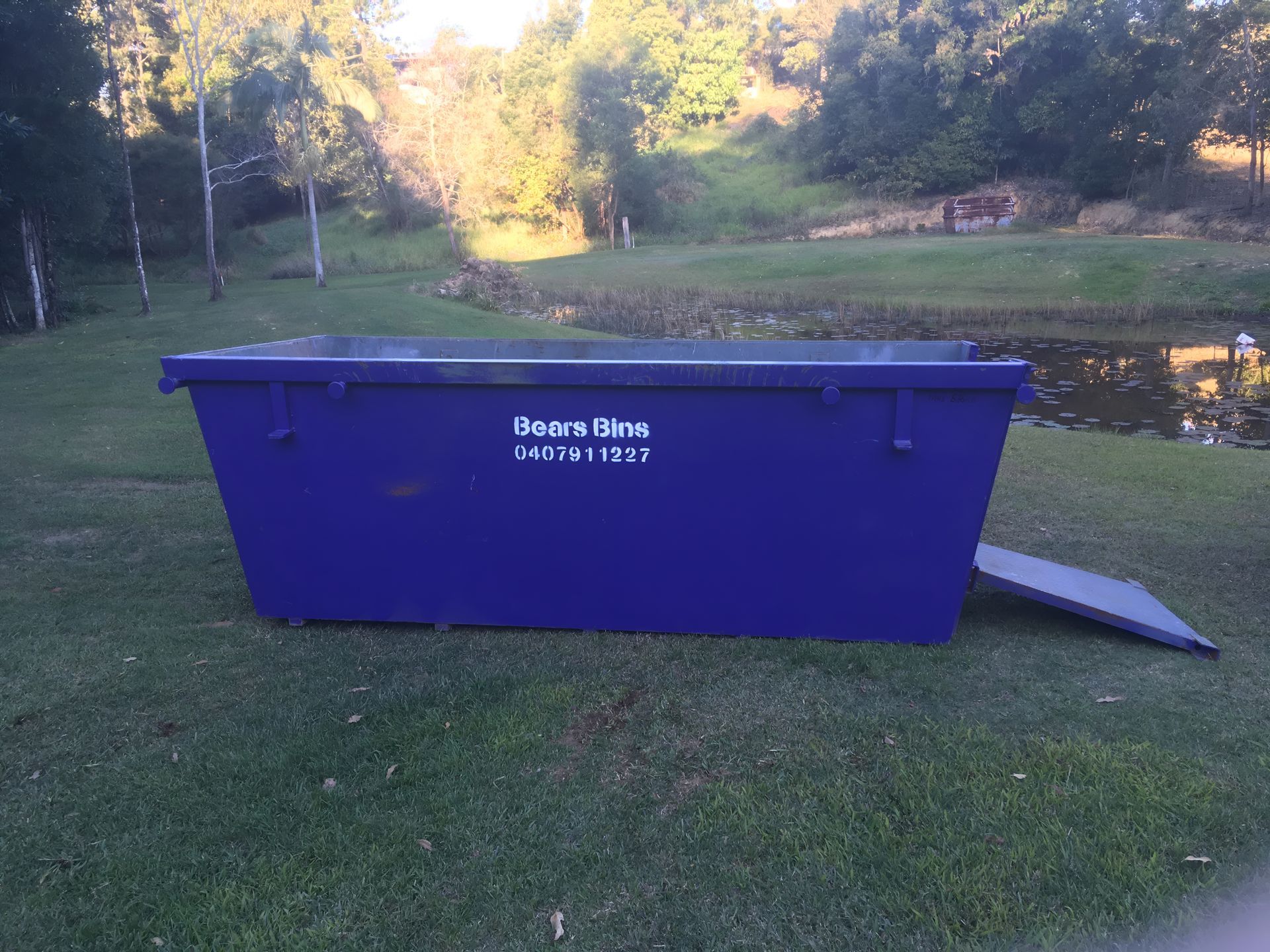 Blue Dumpster on Grass, Near a Pond With Trees in the Background — Skip Bin Hire Sunshine Coast in Kin Kin, QLD