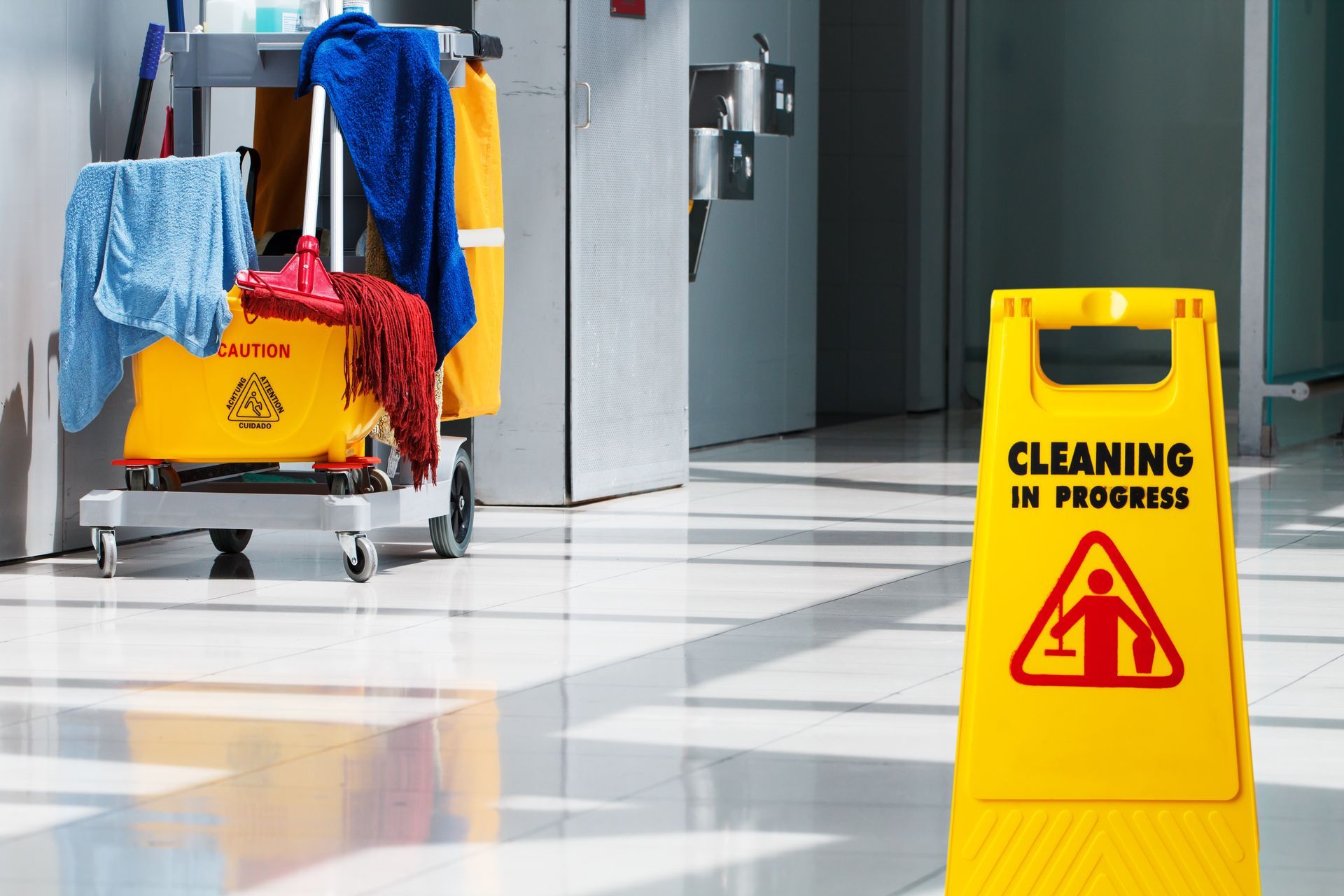 A cleaning cart in front of the office lobby bathrooms with a cleaning in progress sign on display.