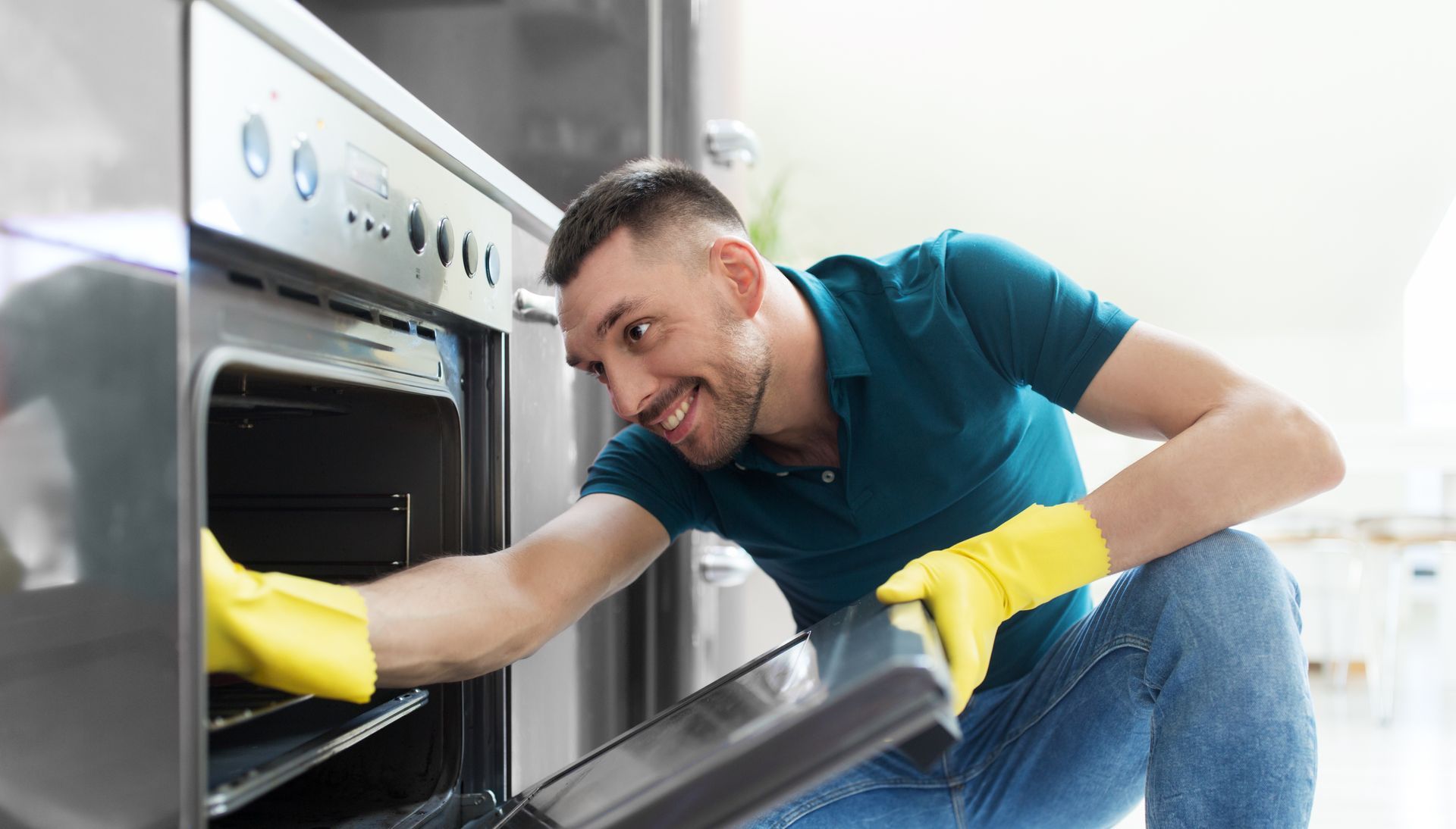 a man in rubber gloves cleaning a dirty stove in a kitchen.