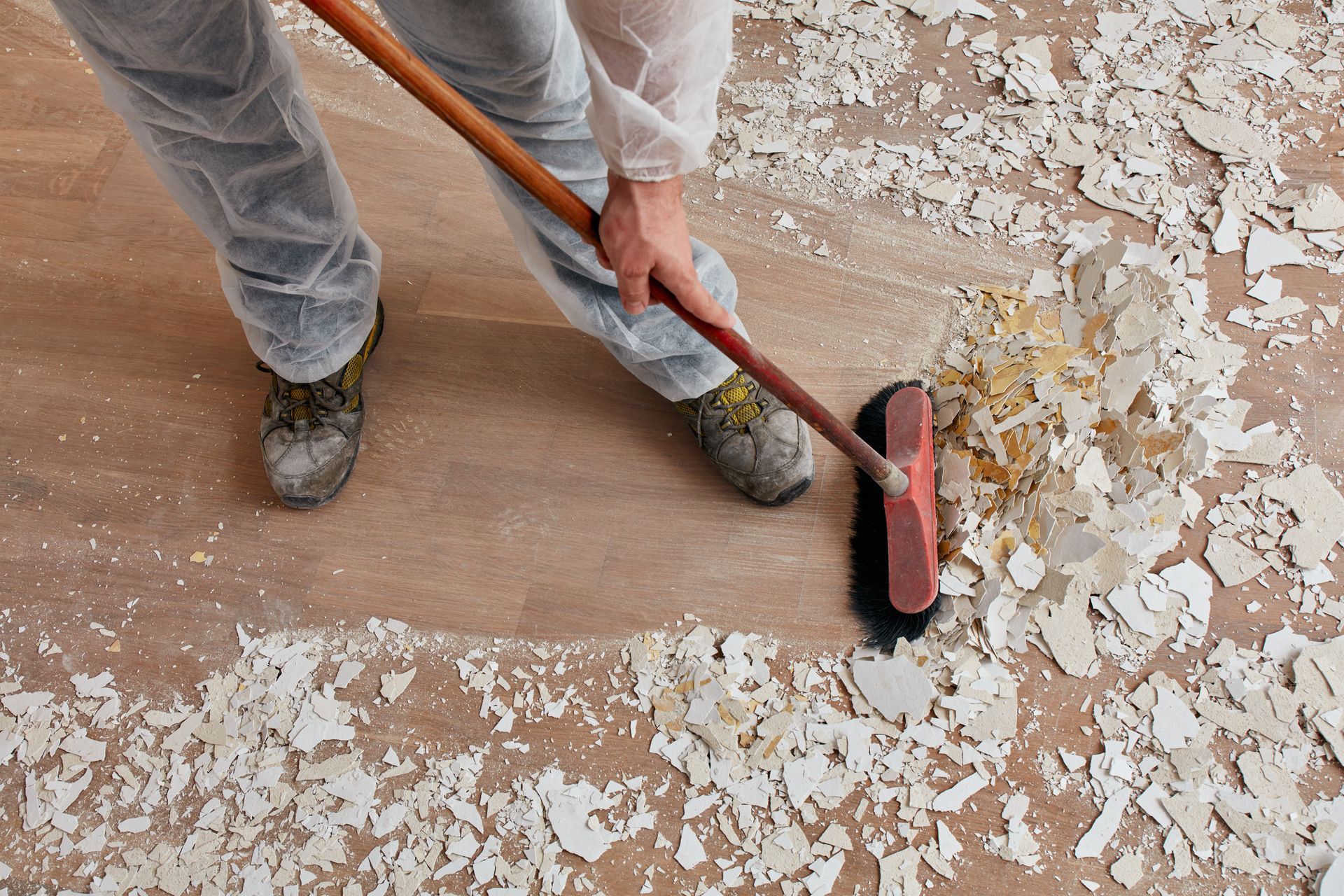 A man sweeping up construction debris from the nice wood floor after a construction project.