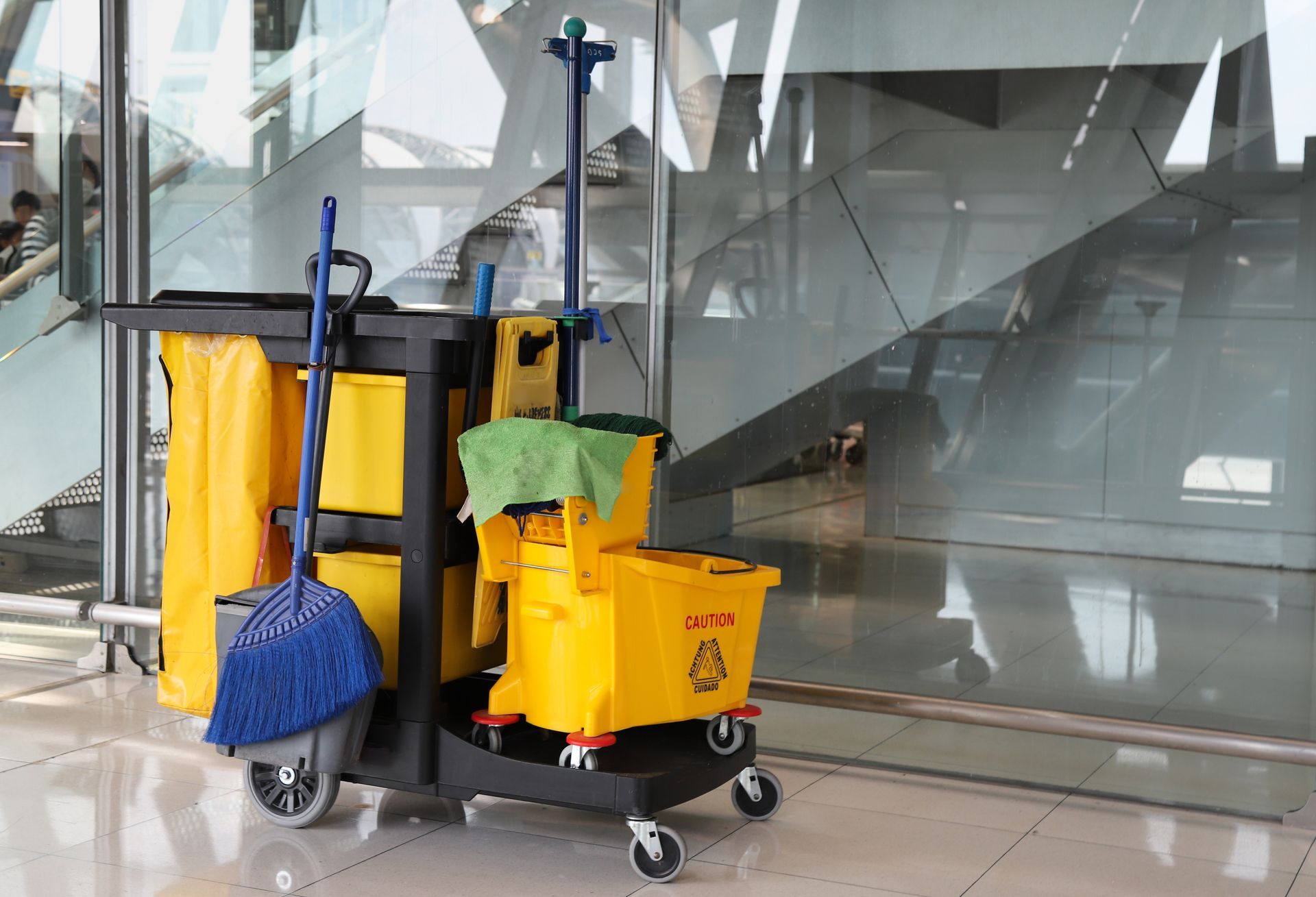 A cleaning cart with broom, dust pan, mop, and bucket sitting in a freshly cleaned lobby next to the stairway.