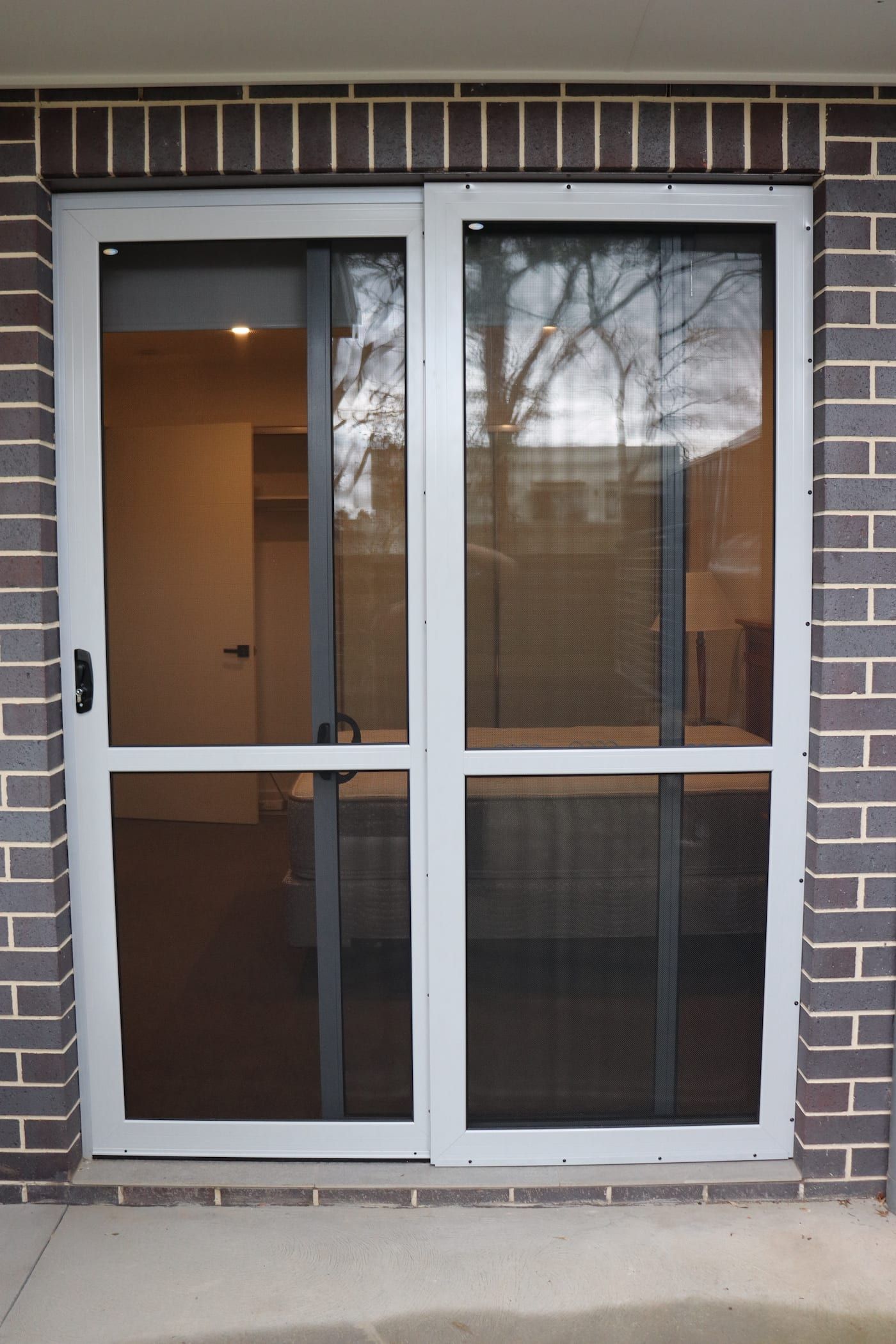 A white sliding glass door with a brick wall behind it