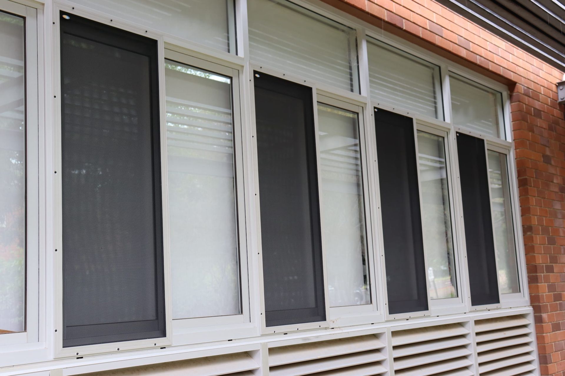 A row of windows with screens on them on a brick building.