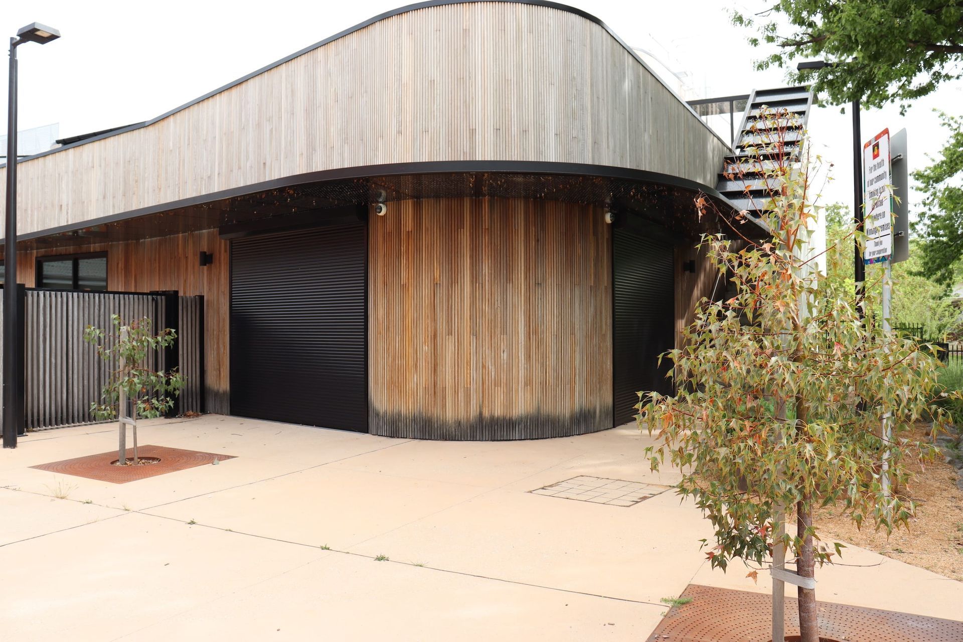 A large wooden building with a black garage door and a tree in front of it.