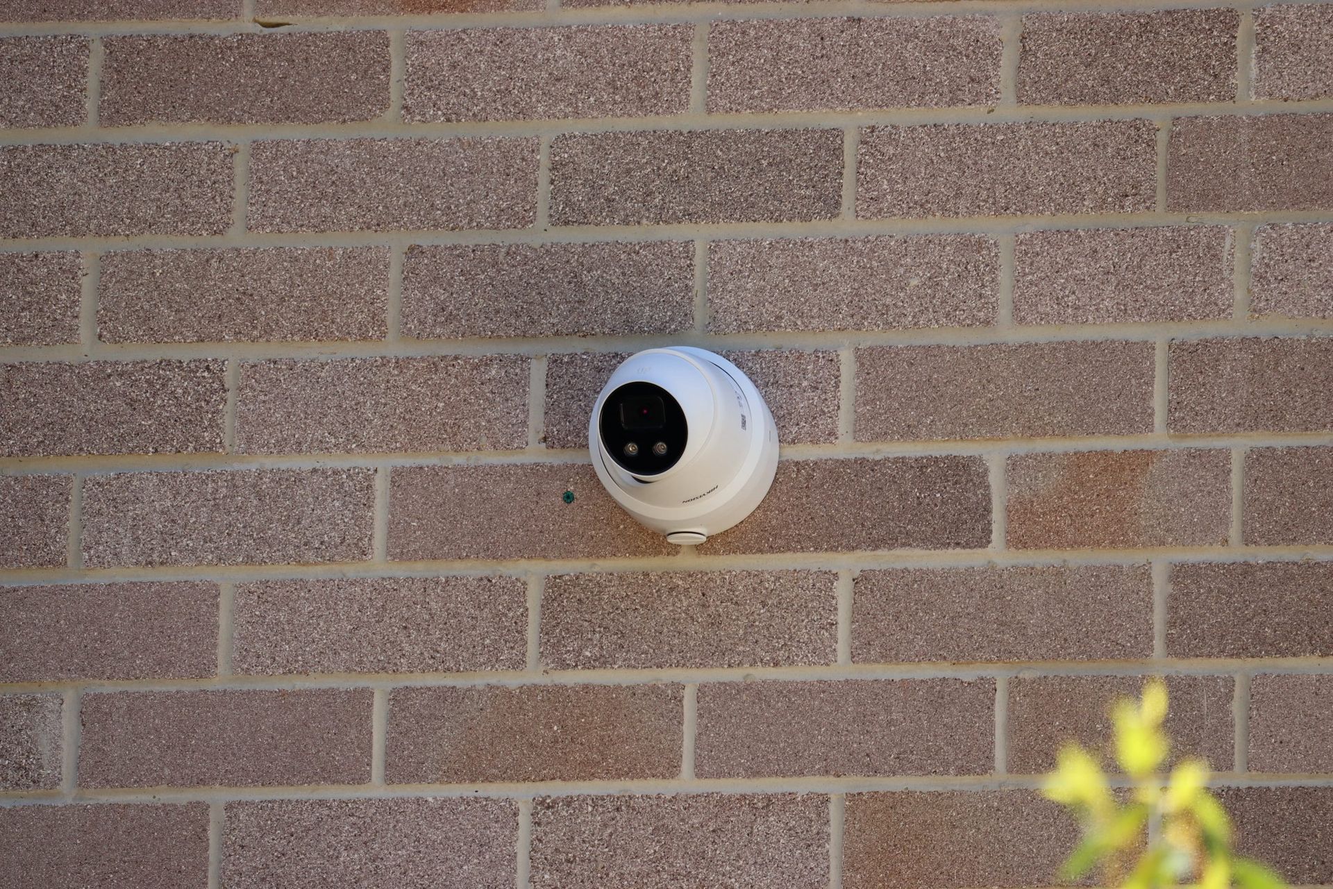 A white camera is mounted on a brick wall.