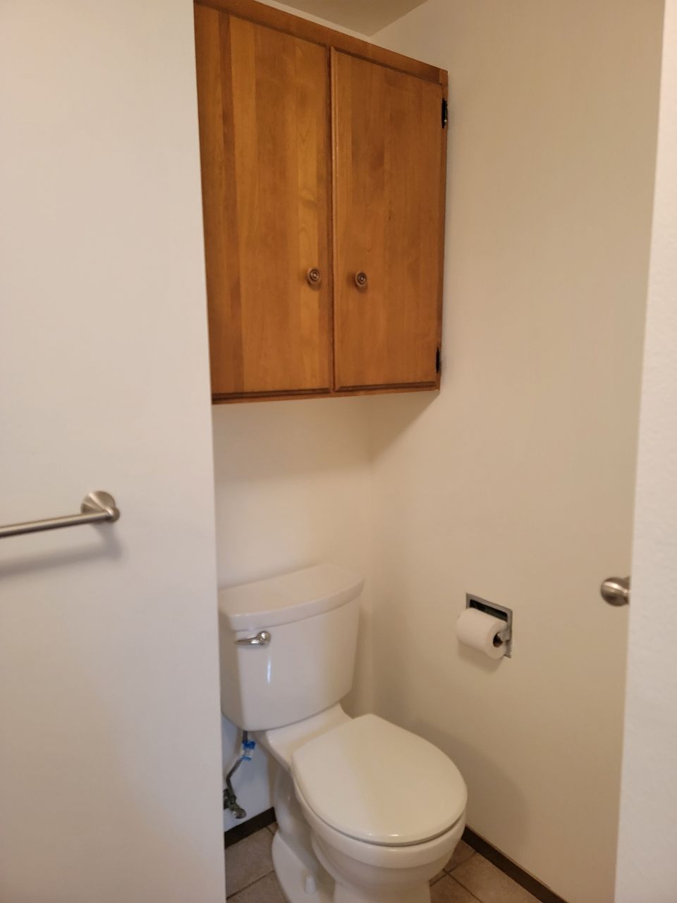 Toilet in a small bathroom, with cabinet above.