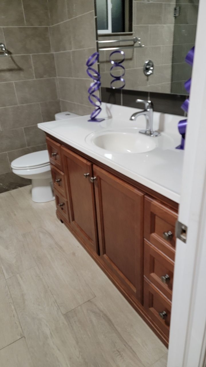 Bathroom with a brown vanity, white countertop, toilet, and gray tile.