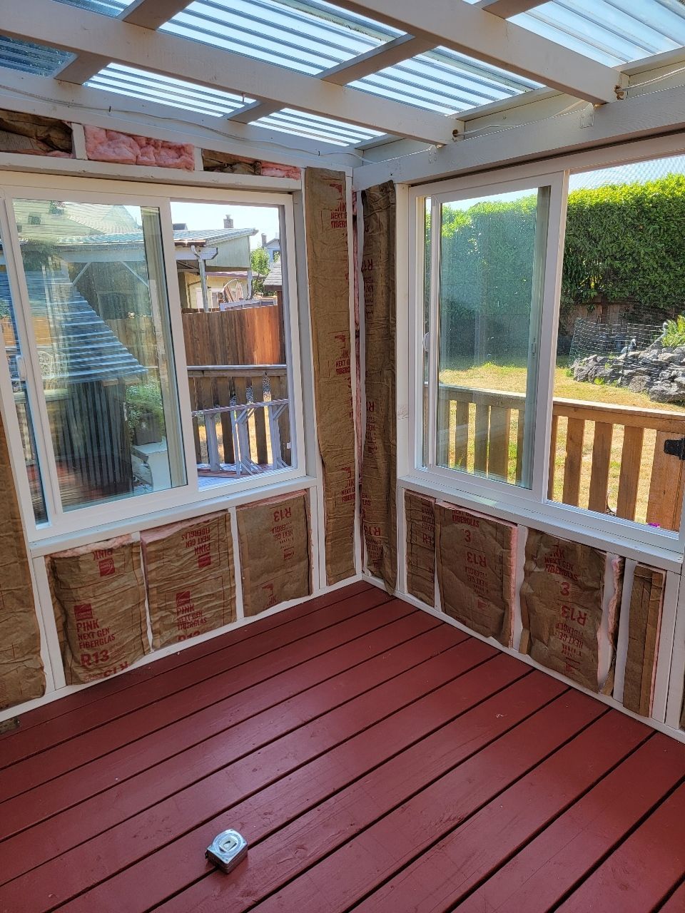 A sunroom with red deck, insulation in walls, windows, and a clear roof.