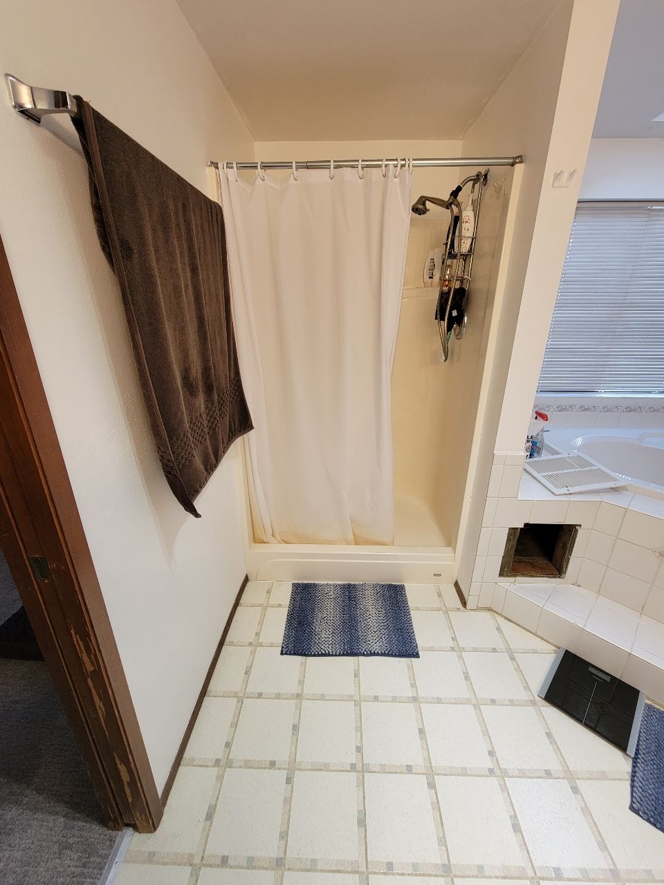 Bathroom with a shower, towel, and blue rug on tile flooring.
