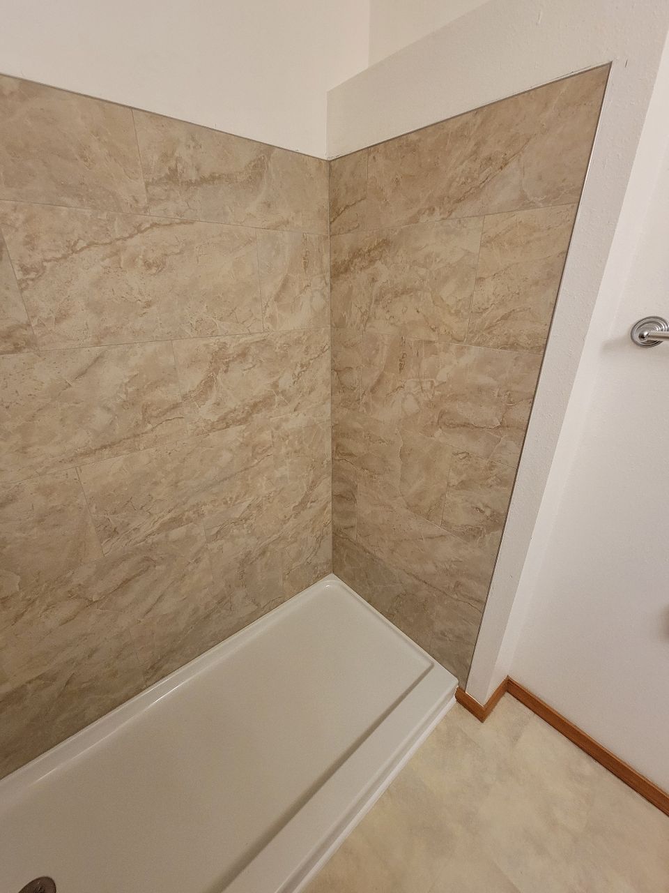 Corner shower with beige marbled walls and white shower base.