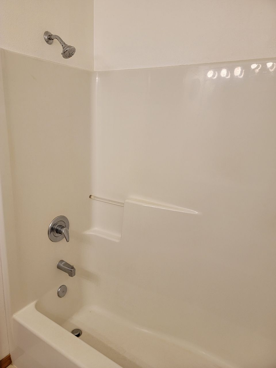 White bathroom shower with faucet, head, and built-in shelf.