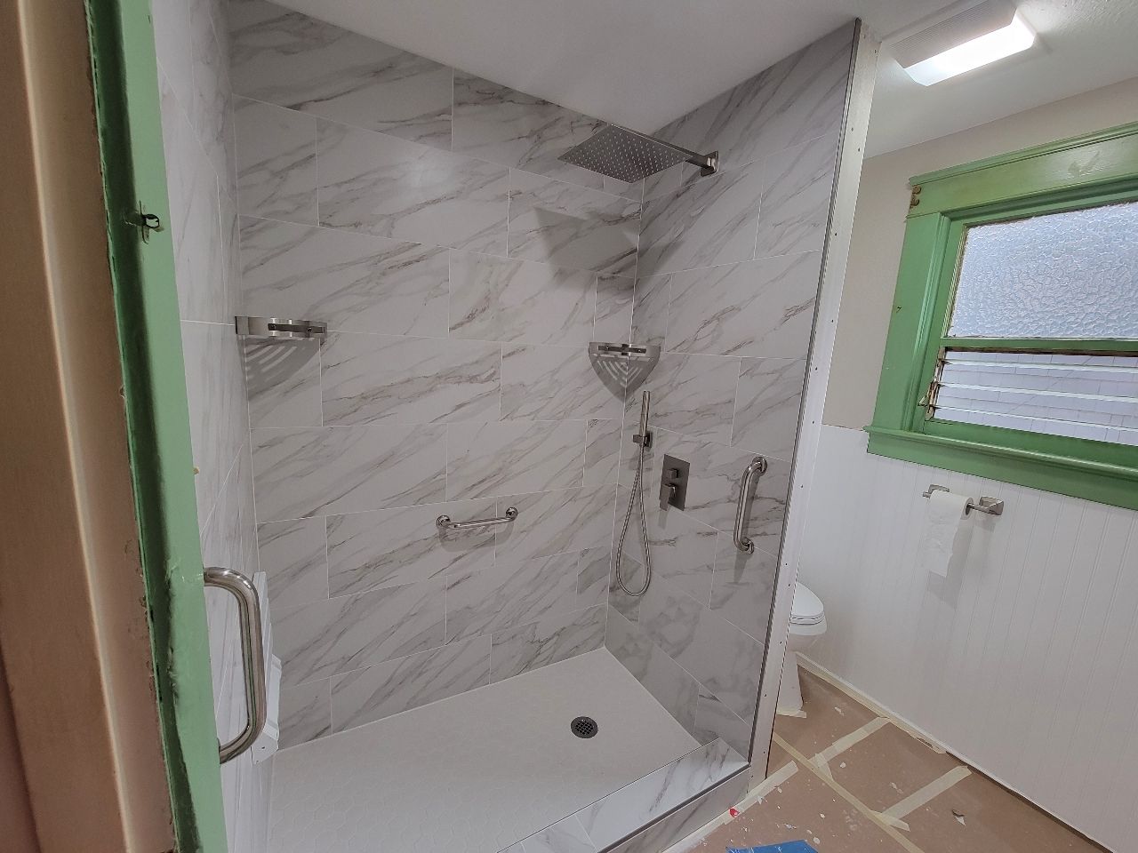Newly tiled shower with glass door in a bathroom, marble pattern, chrome fixtures.
