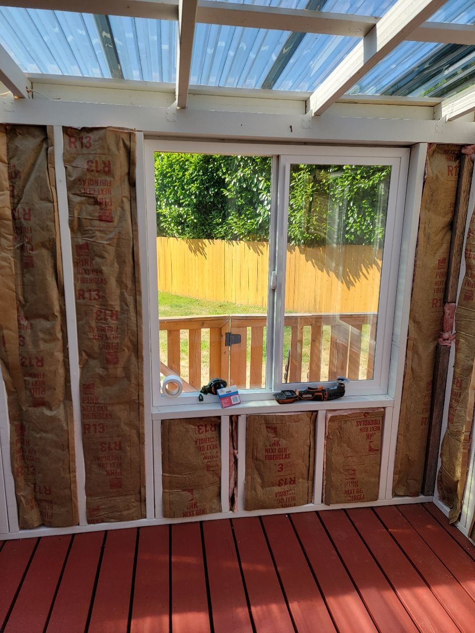 Interior view of a room under construction with insulation, a window, and a red wooden floor.