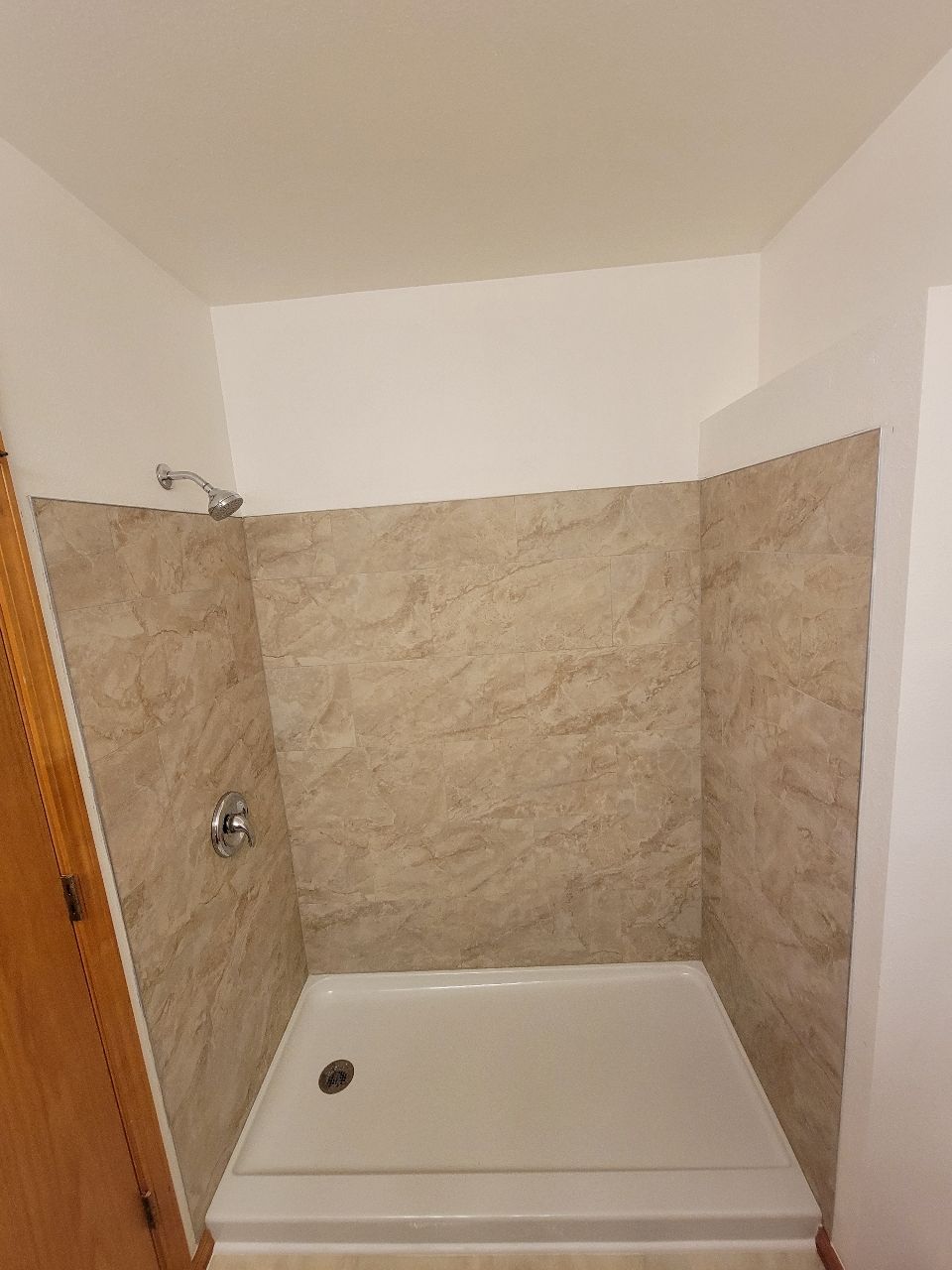 Shower with tan walls, white shower base, and chrome fixtures.