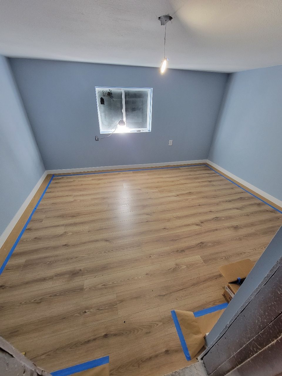 Room with blue walls, light wood flooring, and a small window; recently renovated.