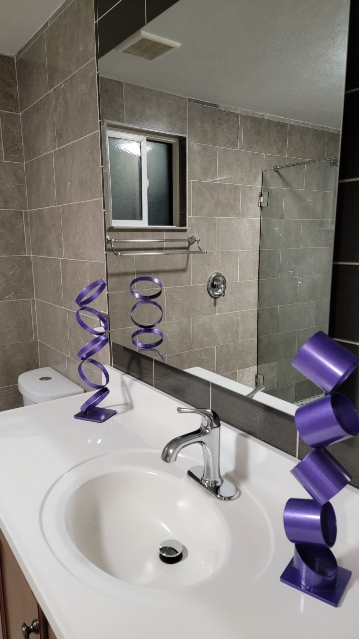 Bathroom with white sink, chrome faucet, purple decorative sculptures, tiled walls, and large mirror.