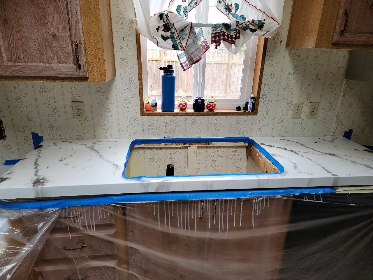 White marble countertop installation in a kitchen. Blue tape, window, and cabinets are visible.