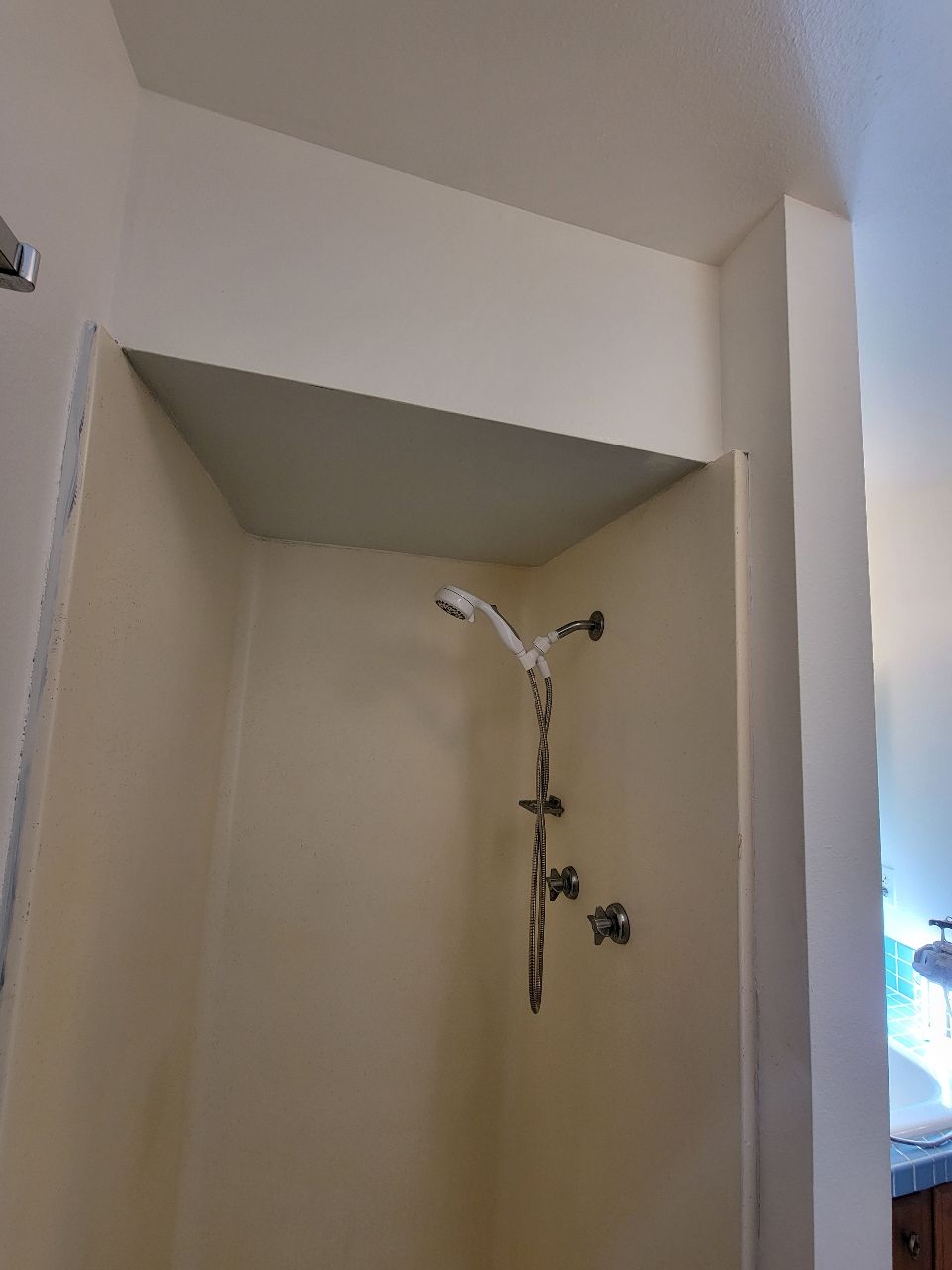 Shower stall with cream-colored walls, chrome fixtures, and a white ceiling panel.