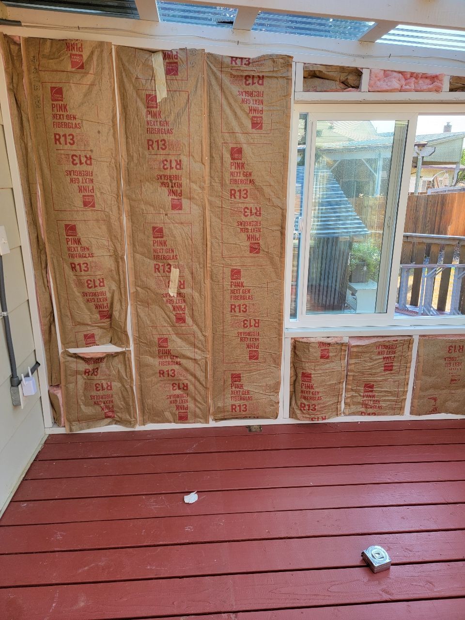 Interior view of room under construction with insulation on the walls and painted red floor.
