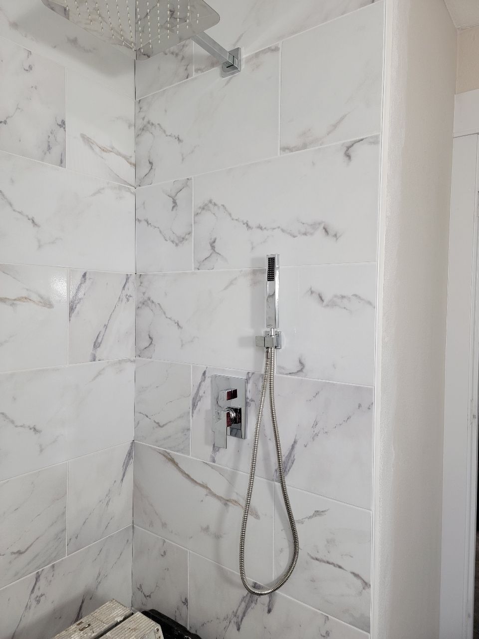 Shower stall with white marble-look tile, chrome fixtures, and a large showerhead.